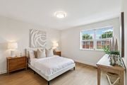 Washington apartment for rent - A bedroom with a large bed, a nightstand with a lamp, and a wooden table with a plant on it.