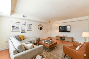 Washington apartment for rent - A living room with a grey couch, a brown chair, a coffee table, and a flat screen TV mounted on the wall.