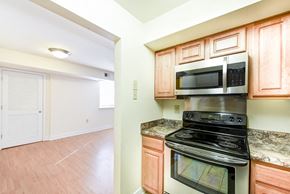 Washington apartment for rent - kitchen with stainless steel appliances and view of living area with wood flooring at jasper place apartments in congress heights washington dc
