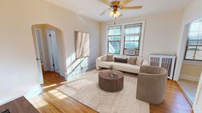 Washington apartment for rent - A living room with a white couch, a brown ottoman, and a ceiling fan.