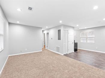The living room is empty of furniture and has white walls and a carpet