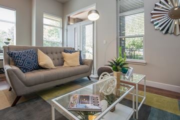 Arvada apartment for rent - A grey couch with blue and yellow pillows sits in a living room with a glass coffee table in front of it.