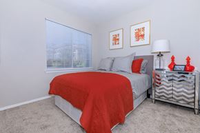 Arvada apartment for rent - A bedroom with a bed covered in a red blanket and a grey blanket on top.