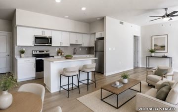 Loveland apartment for rent - A modern kitchen with white cabinets and appliances, a dining table with chairs, and a living area with a couch and coffee table.