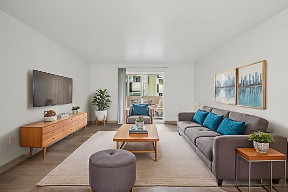 Vancouver apartment for rent - A living room with a grey ottoman, a brown coffee table, a grey couch, a brown side table, a wooden cabinet, a flat screen TV, a potted plant, and a painting on the wall.
