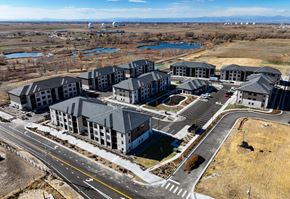 Aurora apartment for rent - A large, modern building complex with a parking lot in front.