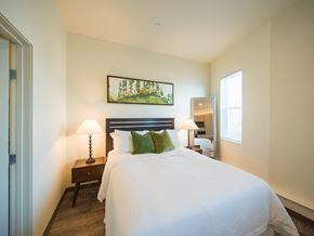 Northglenn apartment for rent - A bedroom with a large bed, a nightstand with a lamp, and a painting on the wall.
