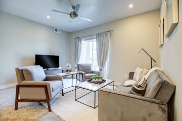 Ft Collins apartment for rent - A living room with a grey couch, a wooden chair, a black television and a fan.
