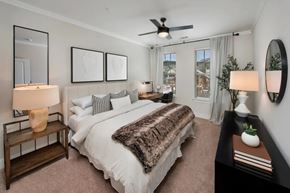 Buford apartment for rent - A bedroom with a large bed, a ceiling fan, and a window with curtains.
