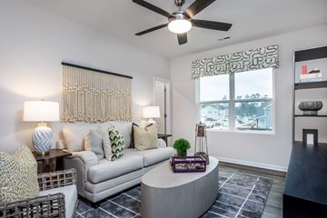 Shallotte townhouse for rent - A living room with a grey couch, a table with a plant and a lamp, and a window with a view of the city.