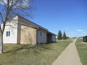 Dickinson apartment for rent - A building with a white and beige exterior is surrounded by a grassy area and a clear blue sky.