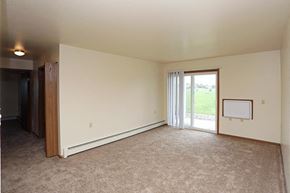 Manitowoc apartment for rent - A large, empty room with a carpeted floor and a sliding glass door leading to a green outdoor area.