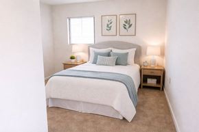 Riverside apartment for rent - A bedroom with a bed, two lamps, and two framed leaves on the wall.