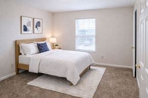Henderson apartment for rent - A bedroom with a bed, two pictures on the wall, a nightstand with a lamp, and a window.