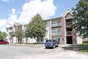 Grinnell apartment for rent - A red car is parked in front of a white building with a balcony.