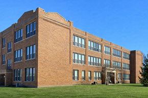 Greenfield apartment for rent - A large red brick building with many windows and a green lawn in front.