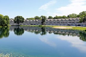 Hartland apartment for rent - A serene lake with a building in the background and a tree in the middle of the lake.