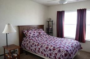 Creston apartment for rent - A bed with a floral patterned comforter sits in a room with a window and curtains.