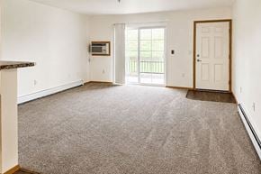 Marshfield apartment for rent - A spacious living room with a carpeted floor and a sliding glass door leading to a balcony.
