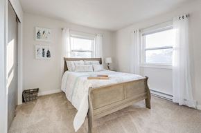 South Bend apartment for rent - A bedroom with a bed, two windows, and a basket on the floor.
