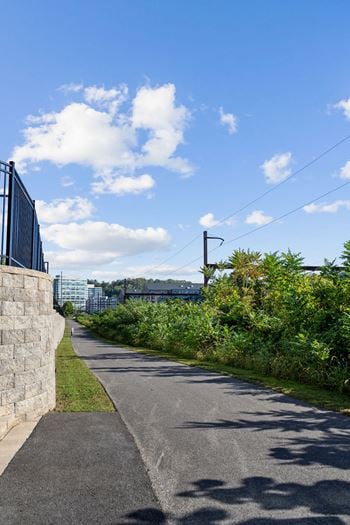 A paved path runs alongside a stone wall with a metal fence on top