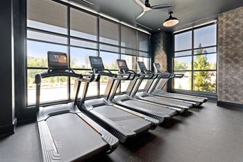 A row of treadmills in a gym with a fan on the ceiling