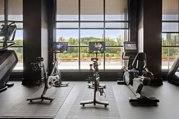 A gym with exercise equipment and a view of the outdoors through the windows