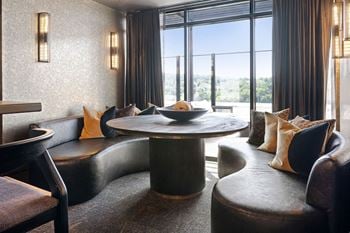 A round table with a bowl of fruit on it is surrounded by black leather chairs