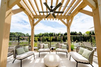 A pergola with chairs and a ottoman on a tile patio