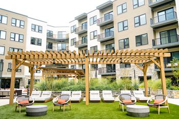 An outdoor lounge area with lounge chairs and a pergola in front of an apartment building