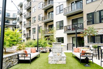An outdoor lounge area with couches and a fire pit in front of an apartment building