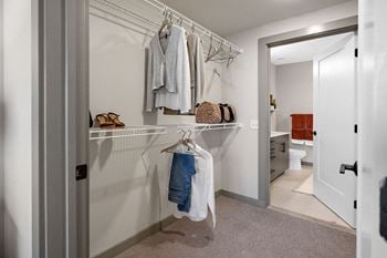 A white closet with clothes hanging and a shelf with a bag on it