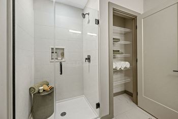 A bathroom with a walk-in shower and a large open door leading to a pantry