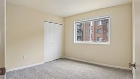 Washington apartment for rent - A room with a carpeted floor, a white door, and a window showing a building outside.