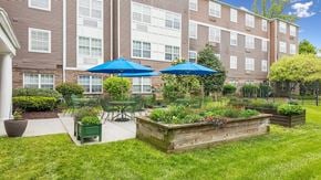 Ellicott City apartment for rent - A large brown wooden planter box with red flowers in the middle of a grassy area.