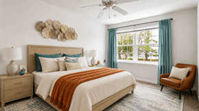 Ellicott City apartment for rent - A bedroom with a large bed, a ceiling fan, and a window with blue curtains.