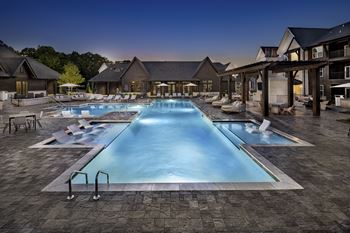 A large swimming pool surrounded by a patio area with chairs and a building in the background