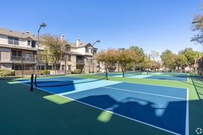 Round Rock townhouse for rent - A tennis court with a blue surface and white lines is surrounded by apartment buildings.