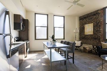 New Orleans apartment for rent - A kitchen with a refrigerator, a dining table with chairs, and a brick wall.