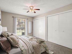 Lafayette apartment for rent - A bedroom with a bed, a ceiling fan, and a window with a view of a fence and trees.