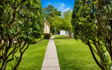 Fayetteville apartment for rent - A pathway leads through a lush green garden to a white building.