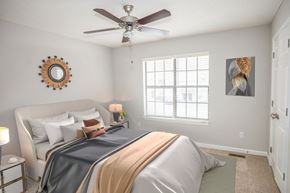 Apex apartment for rent - A bedroom with a bed, a mirror, a ceiling fan, and a window.