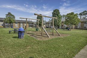 Durham apartment for rent - A playground with a swing set and a blue trash can in front of apartment buildings.