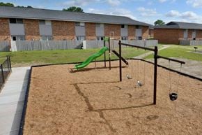 Fayetteville townhouse for rent - A playground with a green slide and swings in front of a brick building.