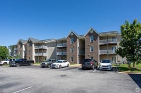 Raeford apartment for rent - A parking lot in front of a multi-story apartment building with cars parked.