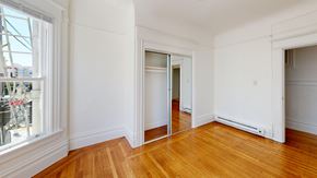 San Francisco apartment for rent - A room with white walls and wooden floors has a large window on the left and a door on the right.