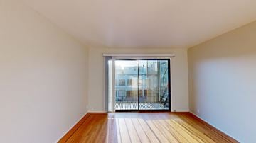 San Francisco apartment for rent - A room with wooden floors and white walls leading to a glass door.