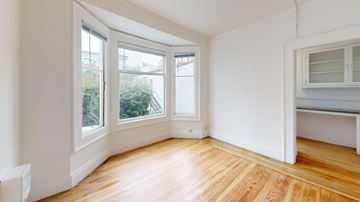 San Francisco apartment for rent - A room with wooden floors and white walls, with a window overlooking a green outdoor area.