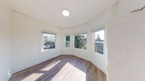 Berkeley apartment for rent - A room with white walls and wooden flooring, with three windows showing an outdoor view.