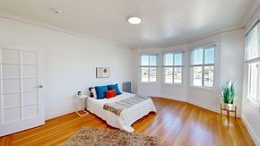 San Francisco apartment for rent - A bedroom with a bed, pillows, a rug, a small table, a potted plant, and a window.